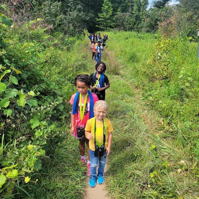 Children hiking on a trail with backpacks and cameras in a natural setting