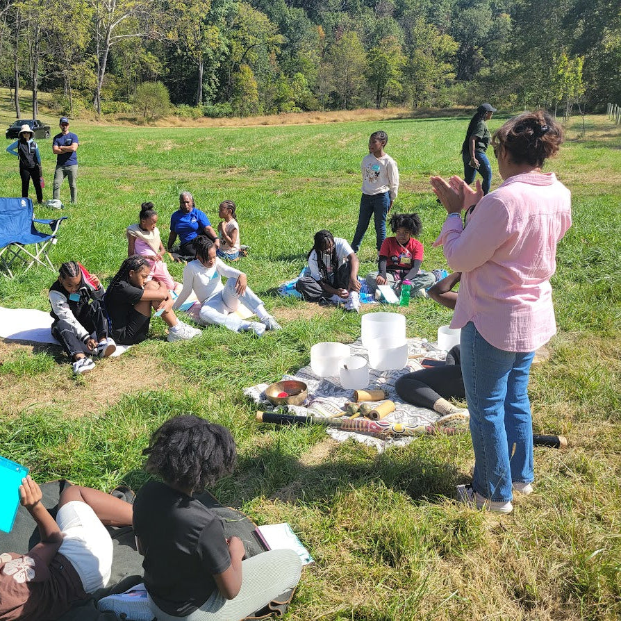 Group of people sitting on blankets in a grassy field with a speaker addressing them.
