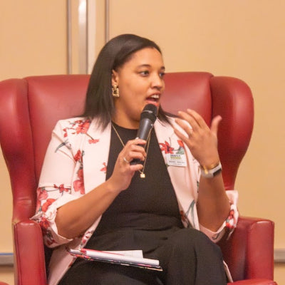 Woman speaking into a microphone while sitting in a red chair.