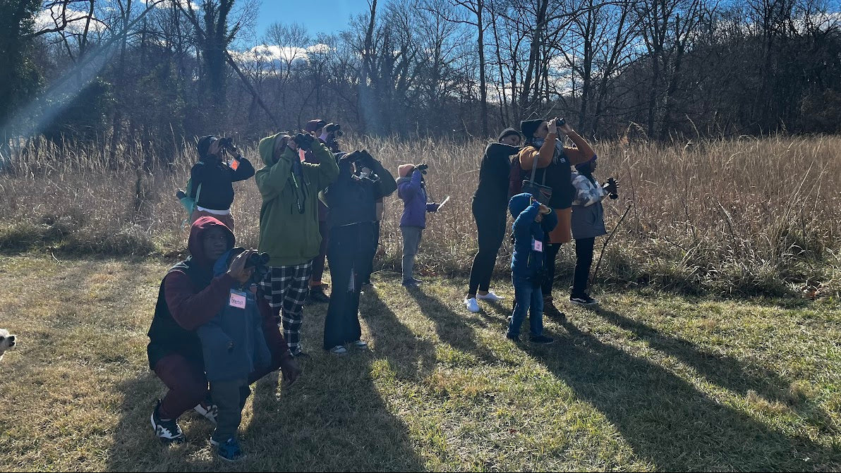 Group of people taking photos in a field with trees and blue sky.