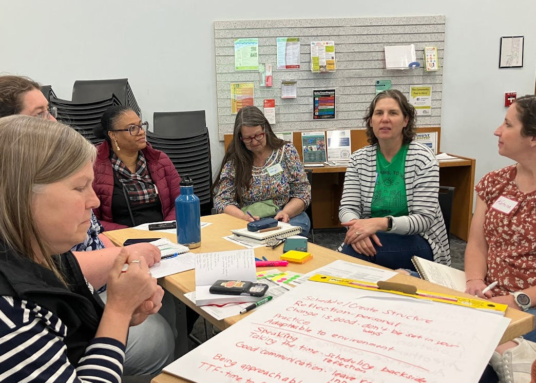 Group of women sitting around a table with papers and pens, engaged in discussion.