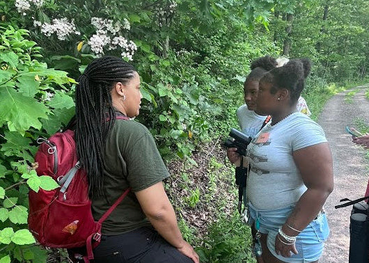 Two women on a nature trail with greenery and a clear sky.