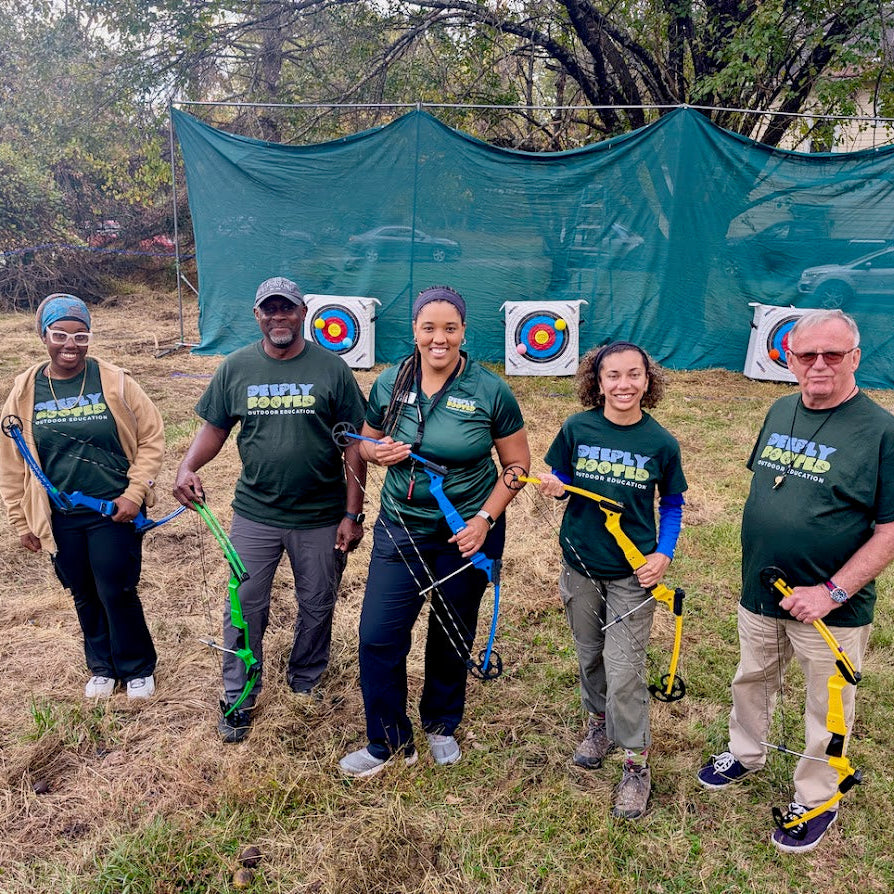 Group of people with archery equipment in a field with a green backdrop