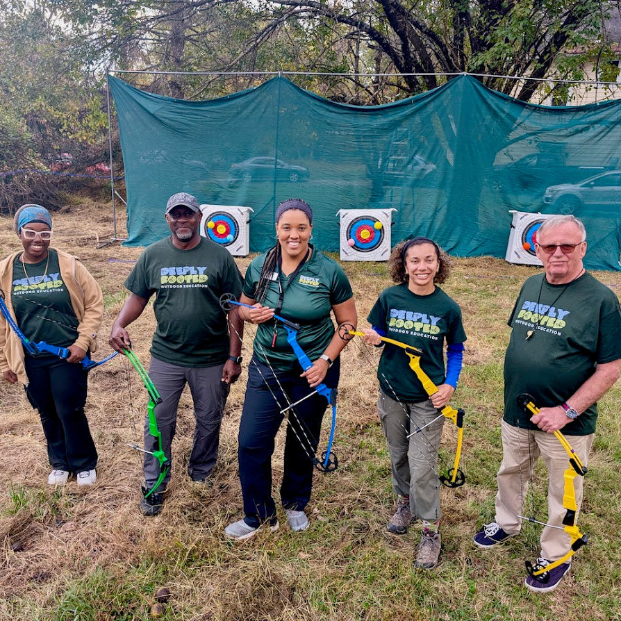 Group of people with archery equipment in a field with a green backdrop