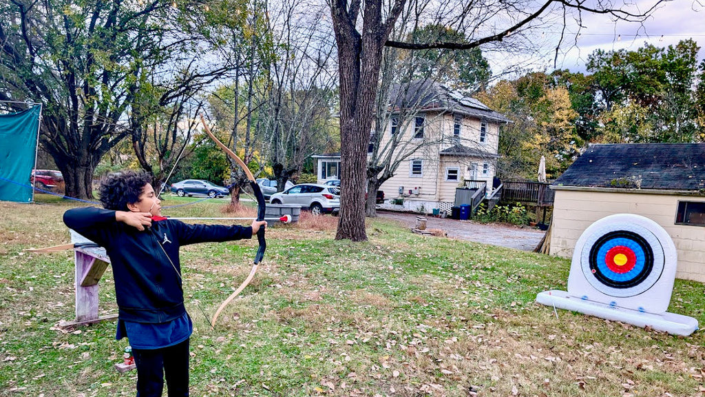 Person practicing archery in a backyard with an archery target.